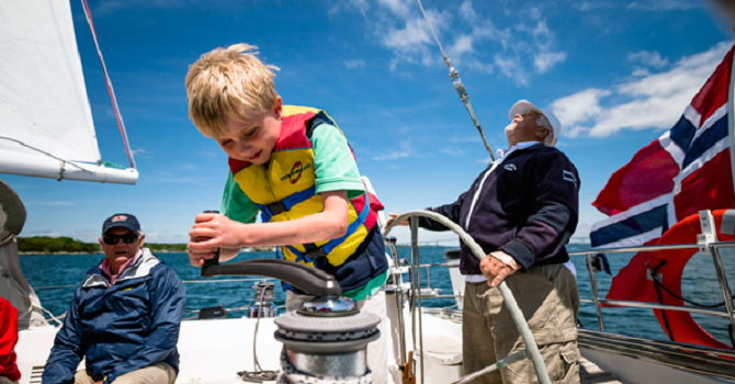 A child turning a winch on a sailboat.